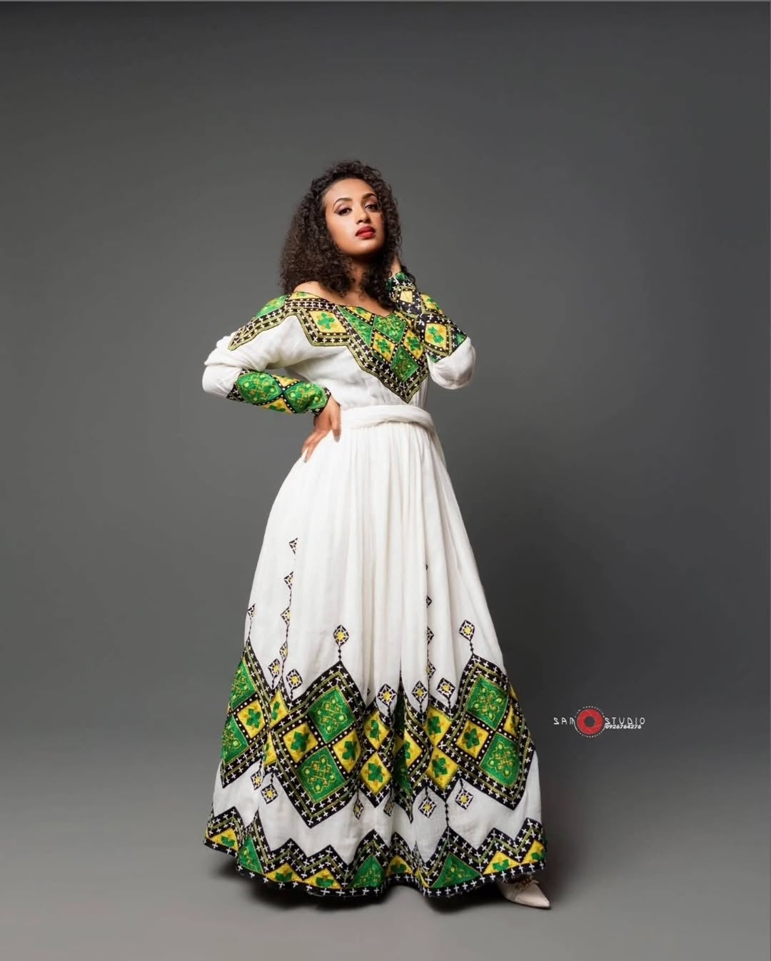 Woman wearing a white Habesha Zuria with green and yellow patterns on a gray background
