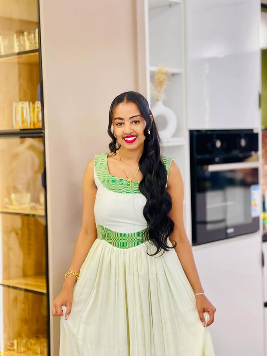 Woman in a white and green  Ethiopian cultural dress standing in a modern kitchen.