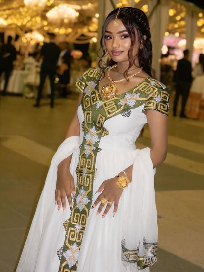 Woman in a white habesha dress with green and gold accents in an indoor setting