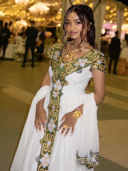 Woman in a white habesha dress with green and gold accents in an indoor setting