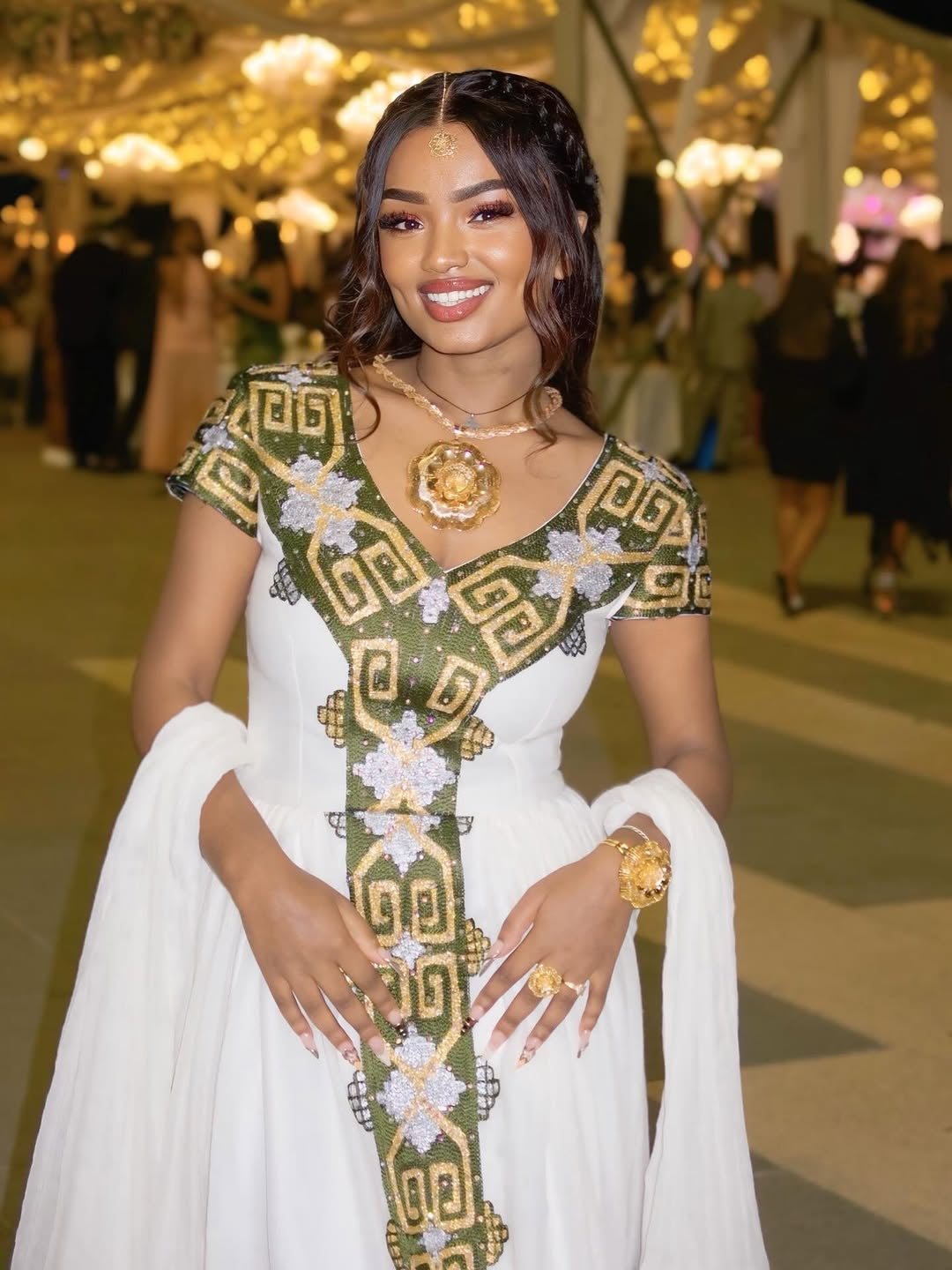 Woman in a white and green embroidered habesha dress at an event with blurred background
