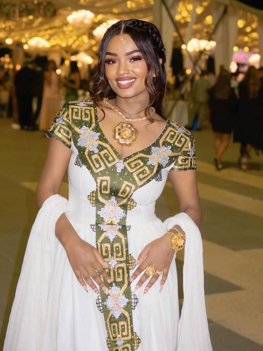 Woman in a white and green embroidered habesha dress at an event with blurred background