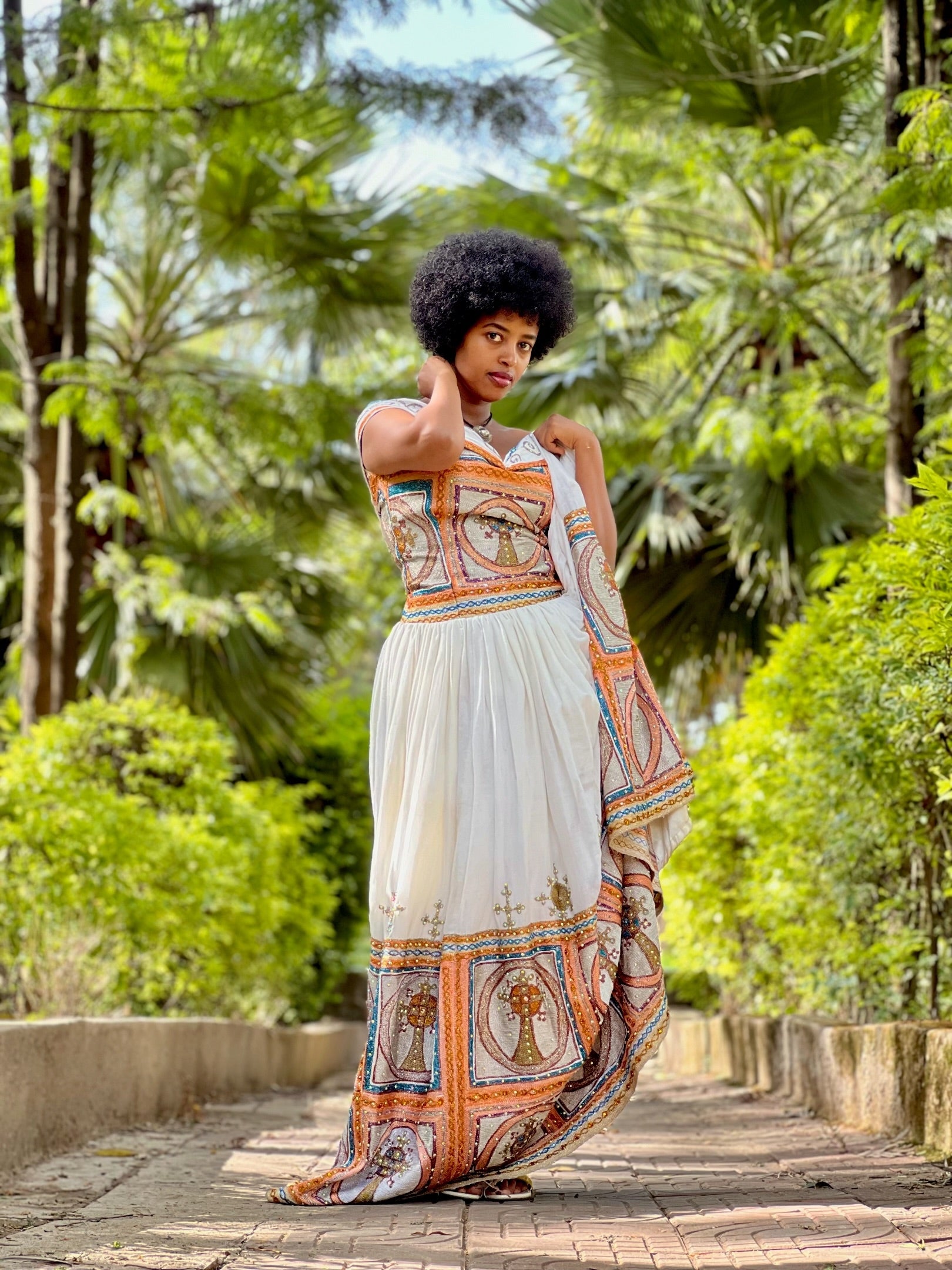 Woman in a long, patterned dress standing in a lush green garden.