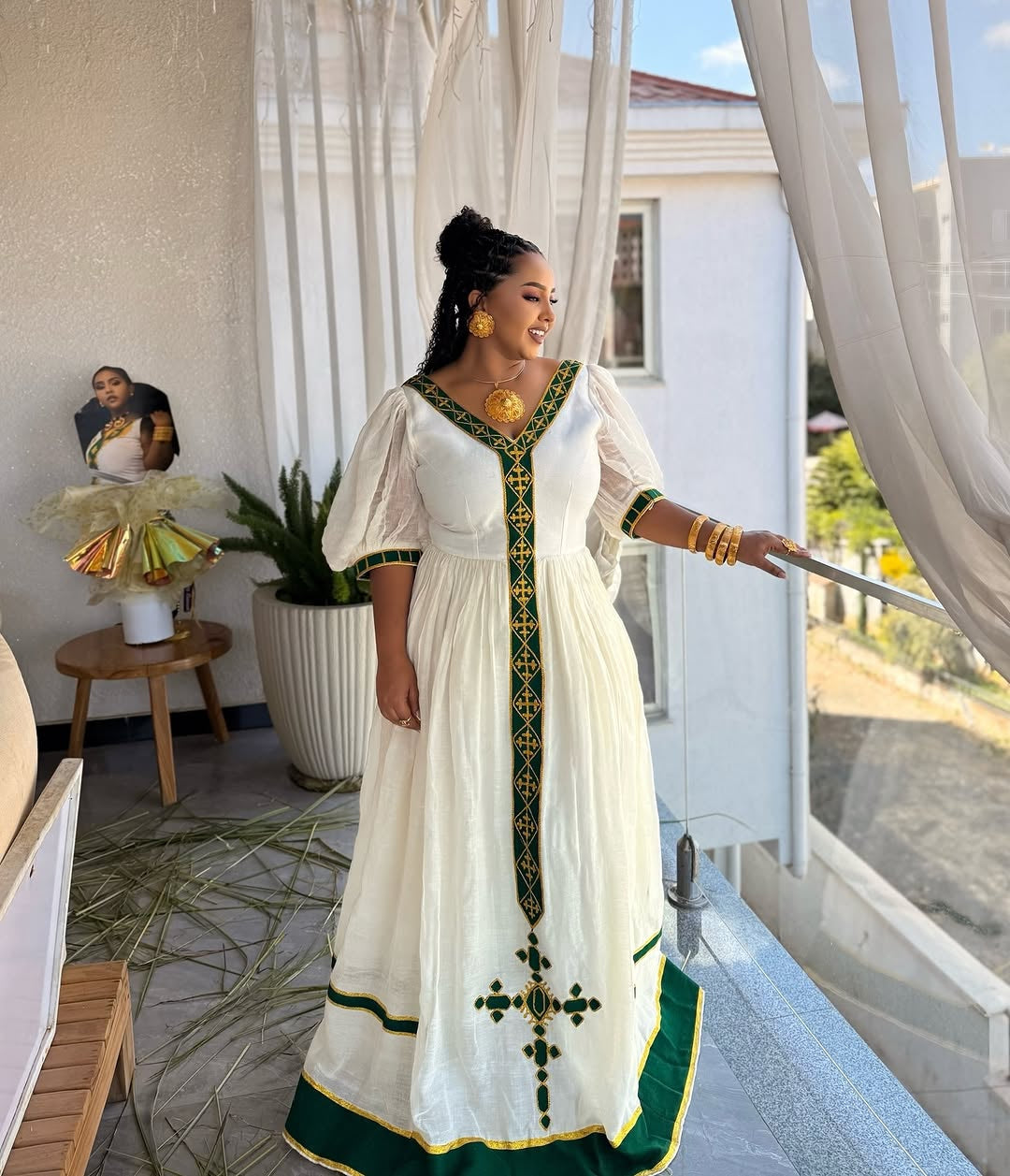 Woman in a white and green traditional Ethiopian dress standing in a room with large windows.