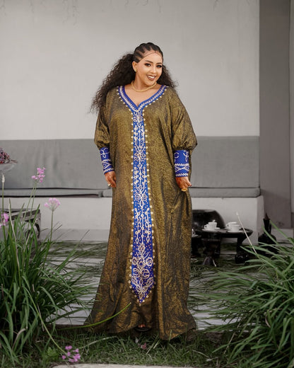 Woman wearing a long, patterned Habesha Ethiopian Dress standing outdoors with plants and a bench in the background.