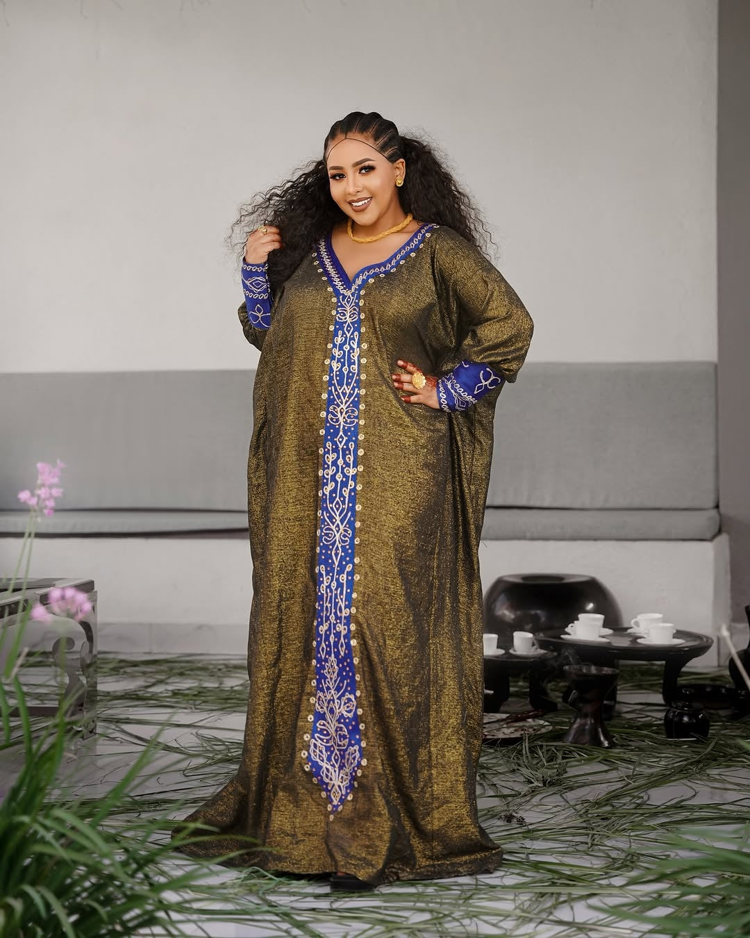 Woman wearing a long, patterned Habesha Ethiopian Dress in a modern living room setting.