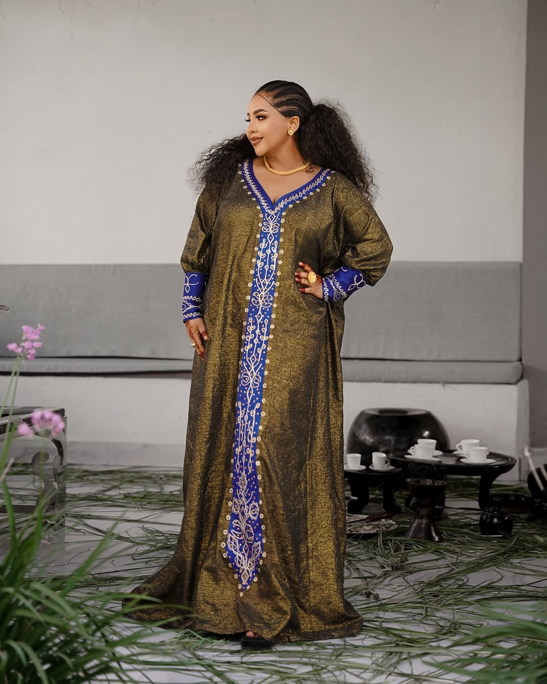 Woman in a long, patterned Habesha Ethiopian Dress standing in an indoor setting with a neutral background.