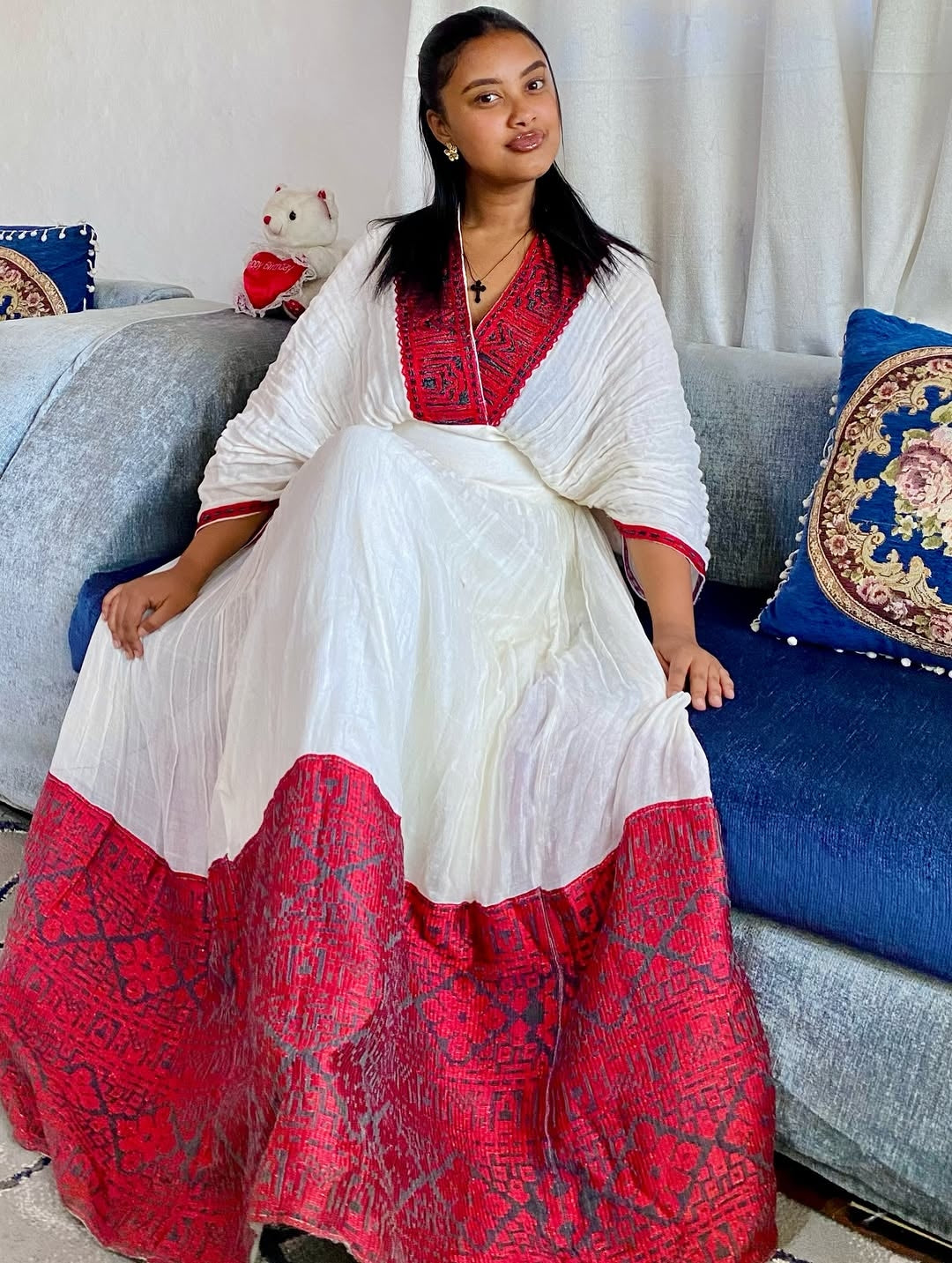 Woman in a white and red traditional Ethiopian dress sitting on a couch with decorative pillows.