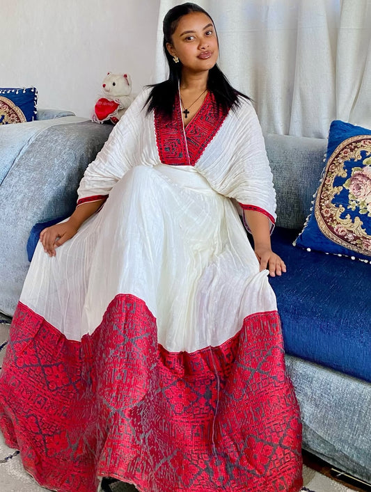 Woman in a white and red traditional Ethiopian dress sitting on a couch with decorative pillows.