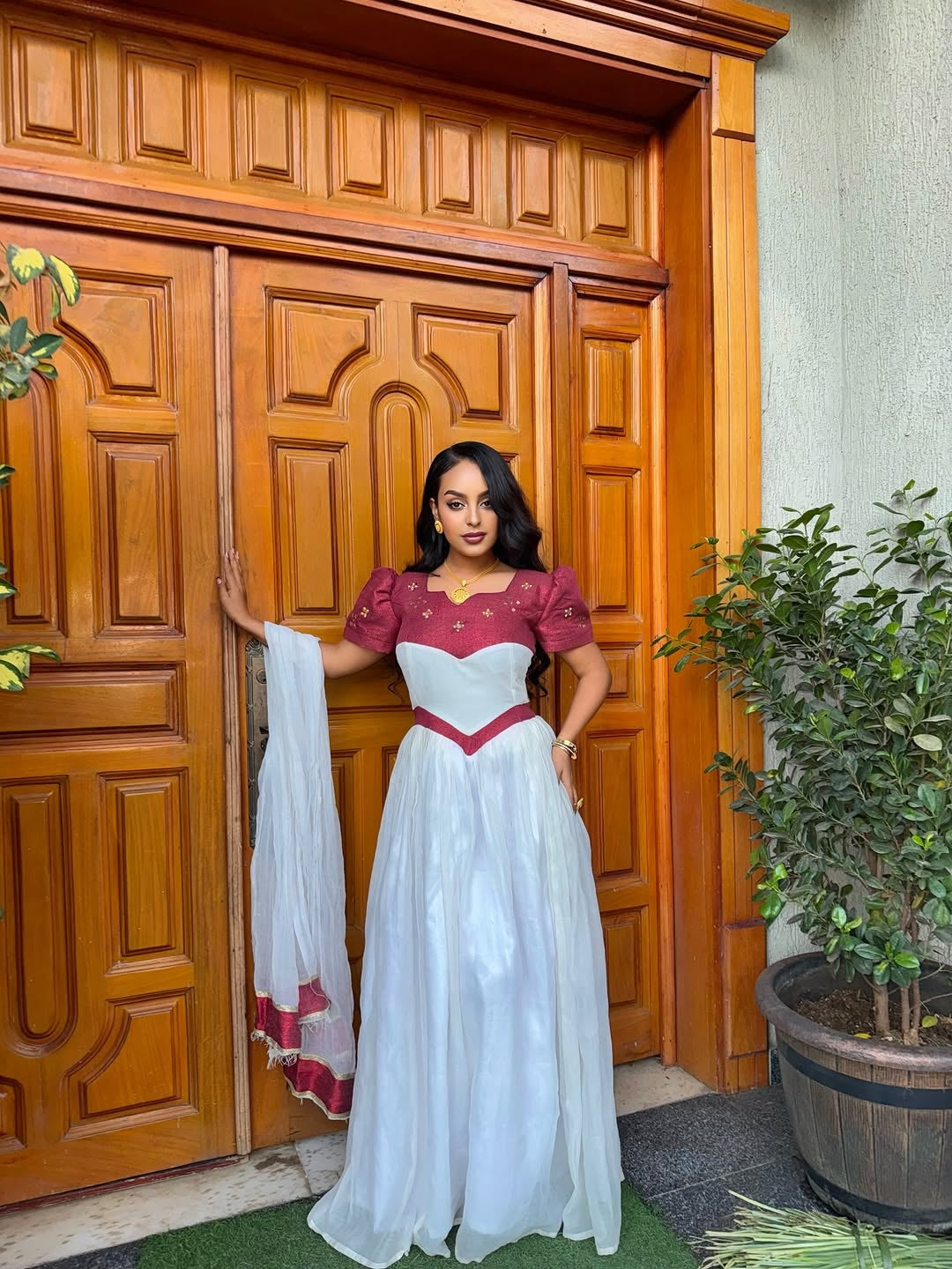 Woman in a red and white traditional Ethiopian cultural dress standing in front of a wooden door.