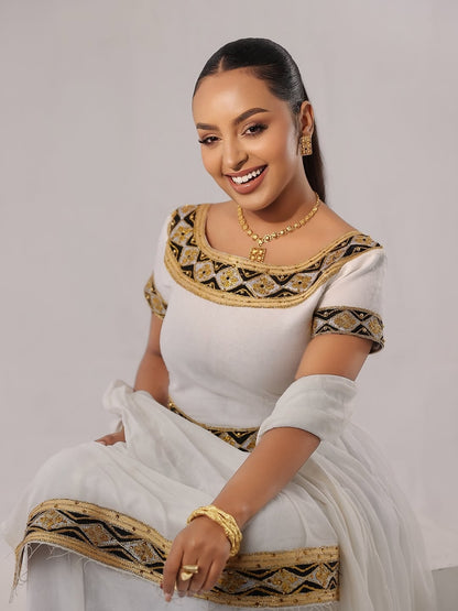 Woman in a Habesha Zuria with gold and black patterns on a plain background