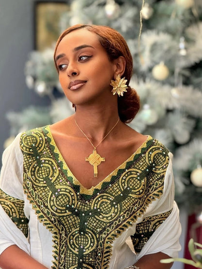 Woman wearing a green and gold embroidered top with a Christmas tree in the background