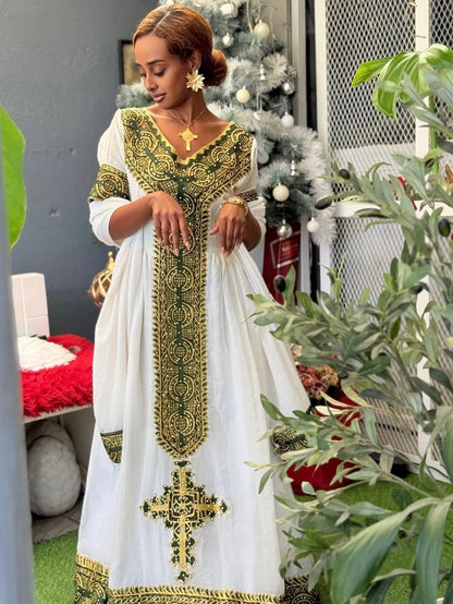 Woman in a white and gold embroidered Habesha Zuria standing in a room with a Christmas tree and plants.
