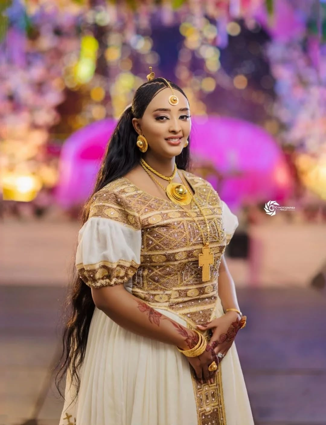 Woman in Ethiopian kemis attire with jewelry against a blurred festive background