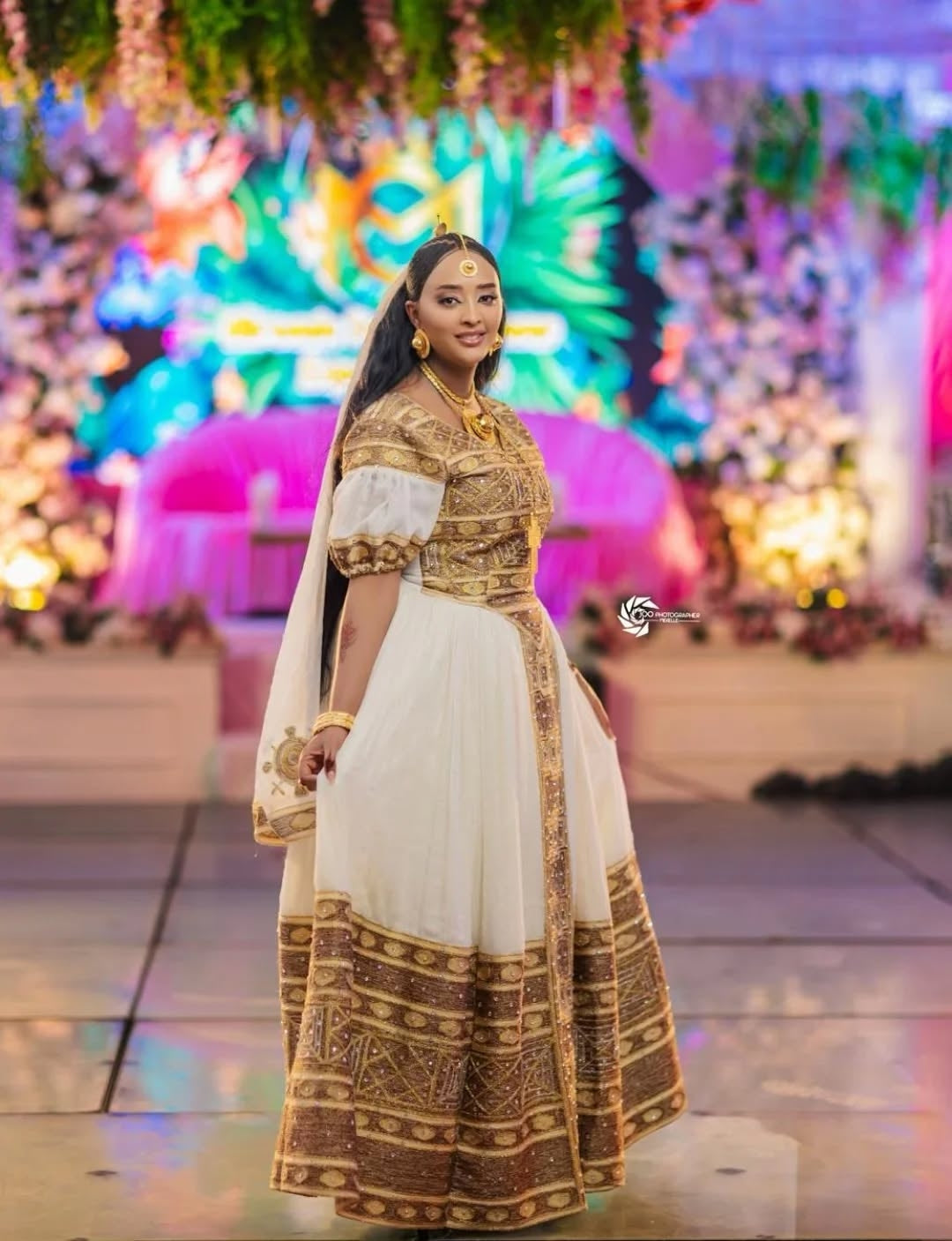 Woman in a traditional gold and white Ethiopian kemis with a colorful, festive background