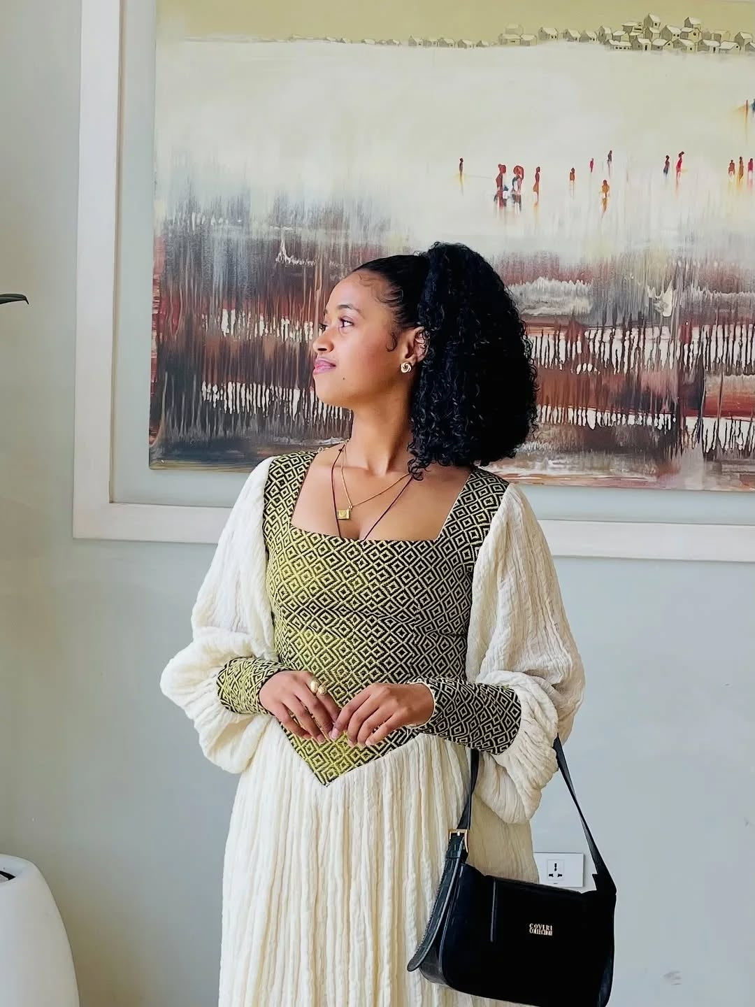 Woman in a green and white habesha dress  standing in front of a painting
