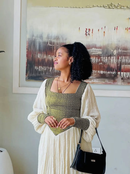 Woman in a green and white habesha dress  standing in front of a painting