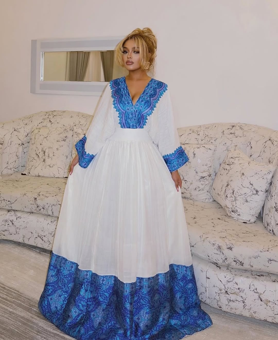 Woman wearing a white and blue Ethiopian cultural dress in a living room setting