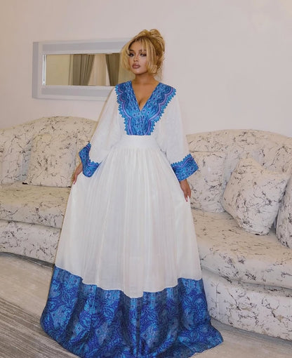 Woman wearing a white and blue Ethiopian cultural dress in a living room setting