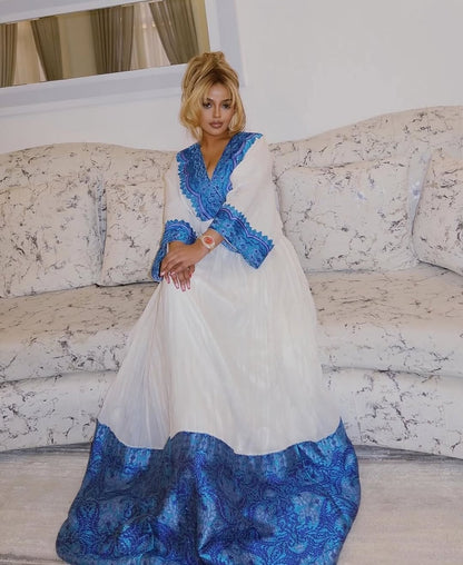 Woman wearing a white and blue Ethiopian cultural dress sitting on a marble-patterned couch.