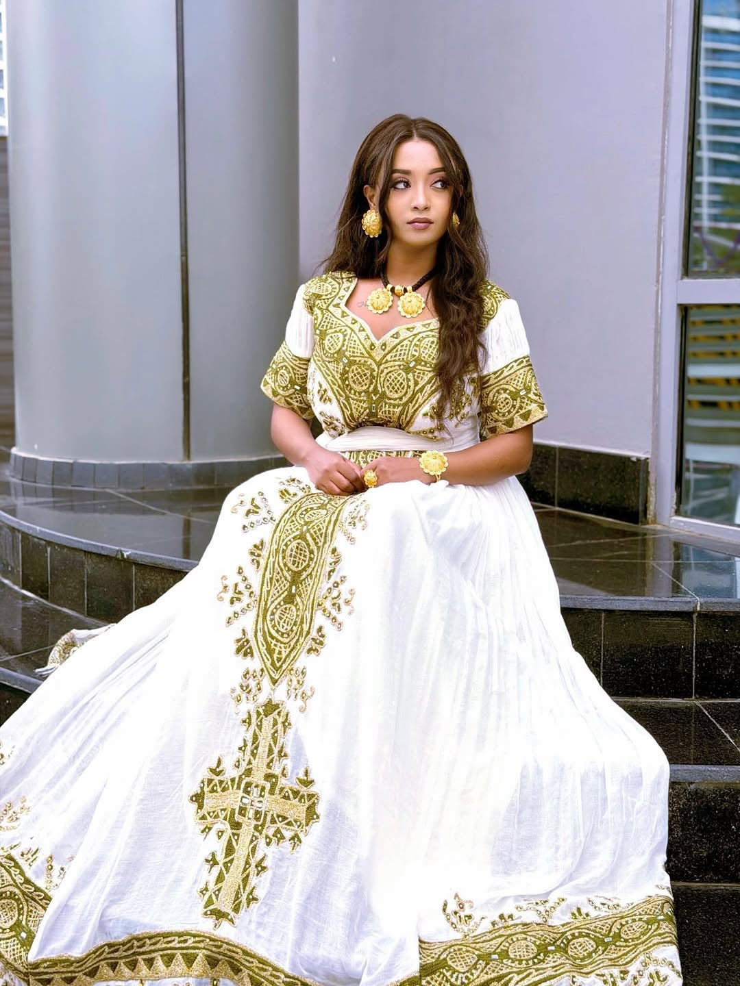 Woman wearing a white and gold traditional Habesha Dress  sitting on steps.