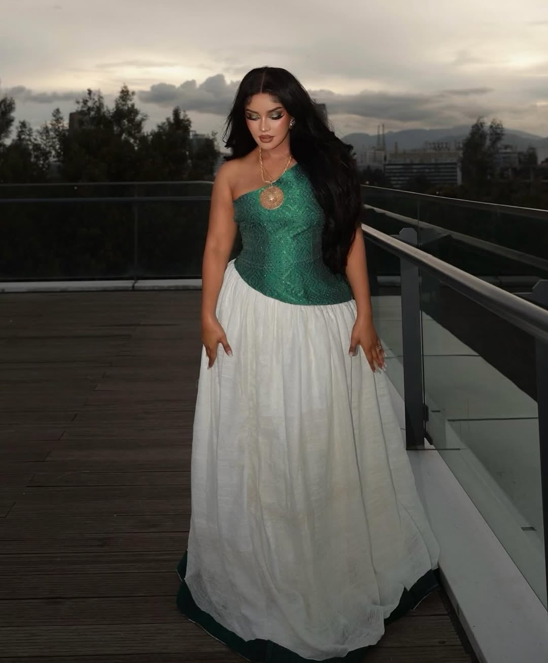 Woman in a green and white Habesha Dress – standing on a rooftop with cityscape in the background