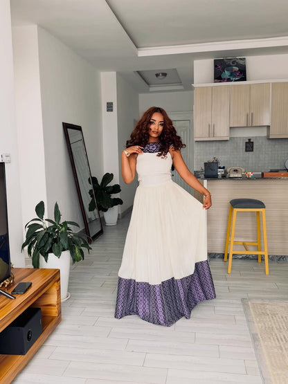 Woman in a white and purple Ethiopian Dress  standing in a modern kitchen.