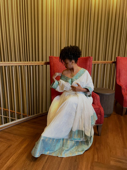 Woman in a long, light-colored dress sitting on a red chair against a textured wall.