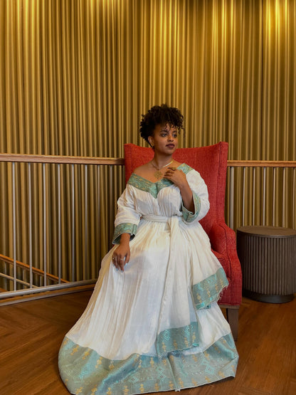 Woman in a white and green dress sitting on a red chair against a gold curtain background