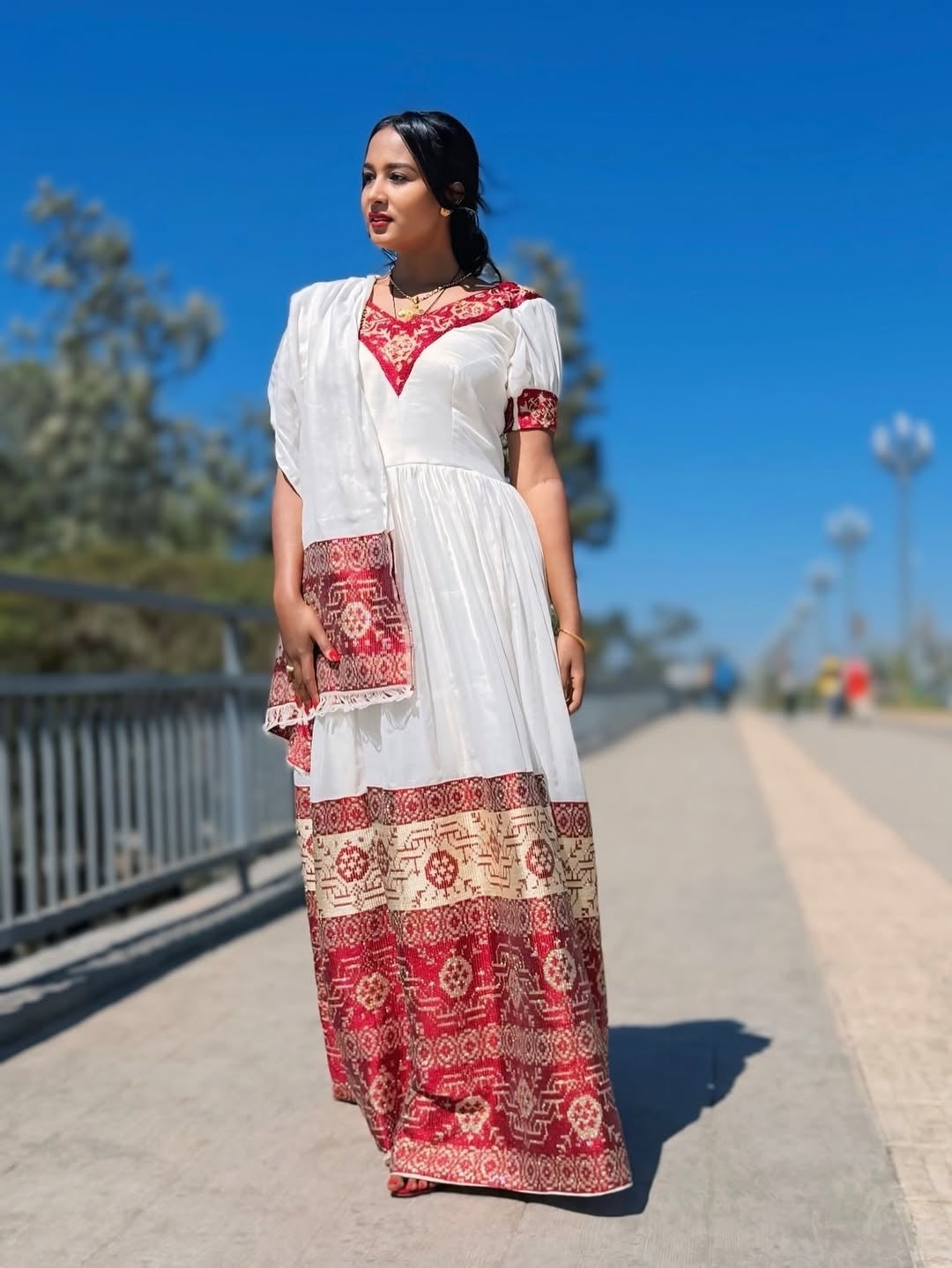 Woman wearing a white and red traditional Ethiopian cultural dress on a sunny day.