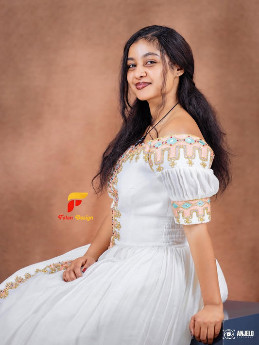 Woman in a white and gold habesha dress in an elegant interior setting.