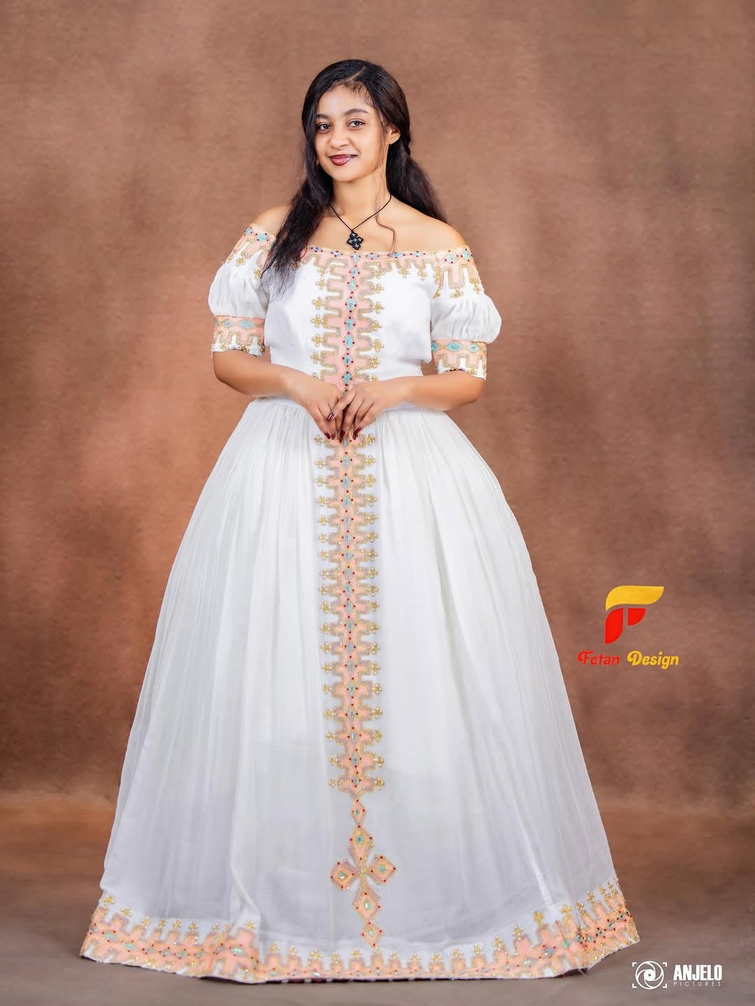 Woman wearing a white dress with gold embroidery against a brown background