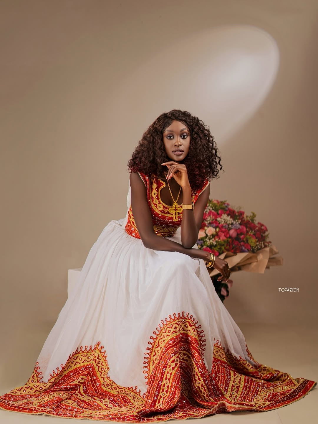 Woman in a traditional Ethiopian cultural dress with floral arrangement on a beige background