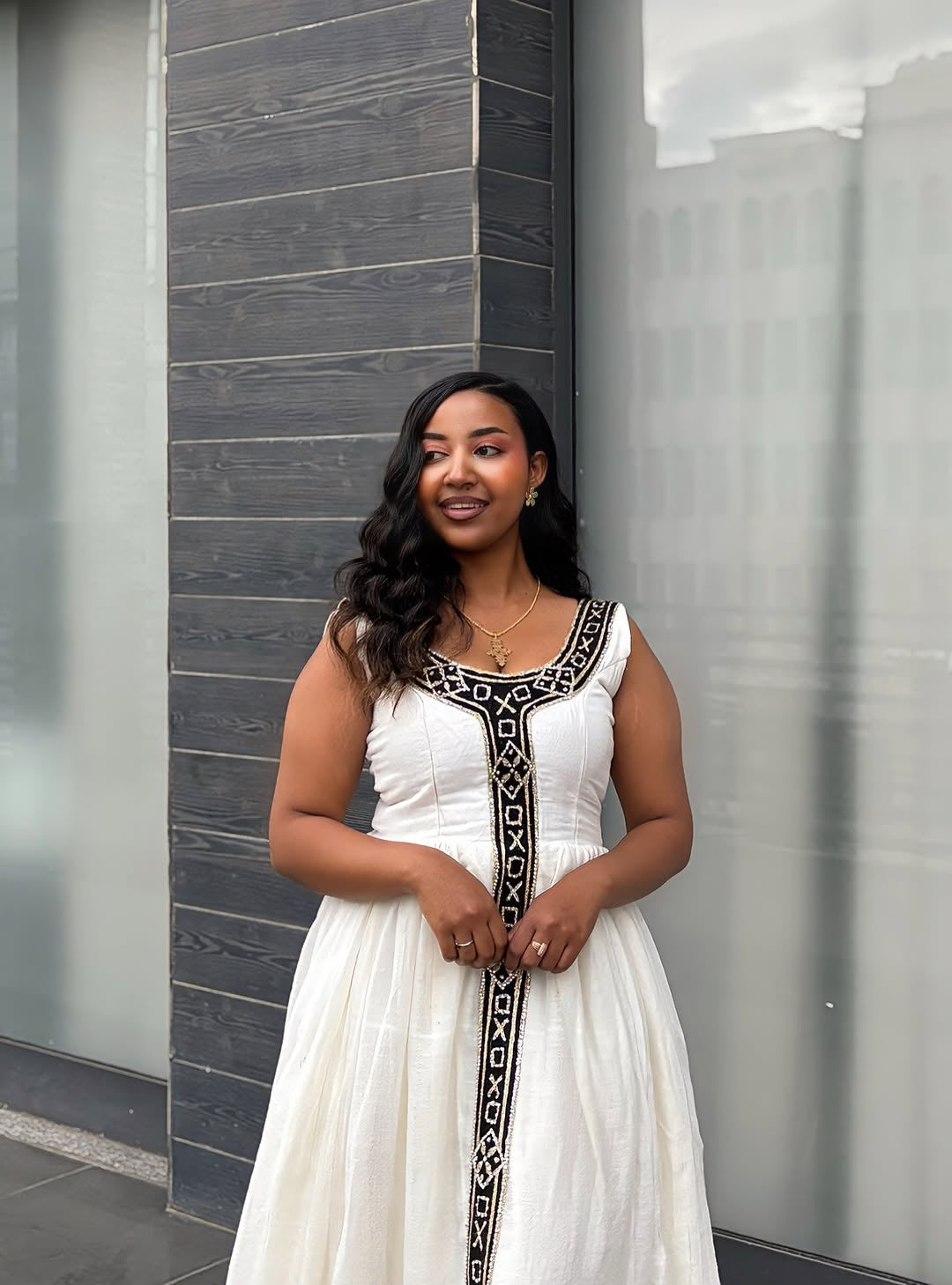 Woman in a white dress with black patterns standing against a modern building.