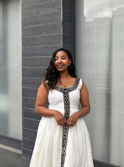 Woman in a white dress with black patterns standing against a modern building.
