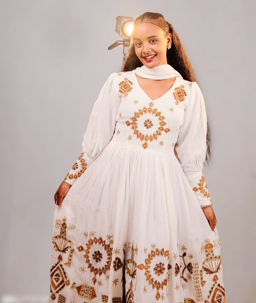 Woman wearing a white Ethiopian traditional dress with gold embroidery against a gray background
