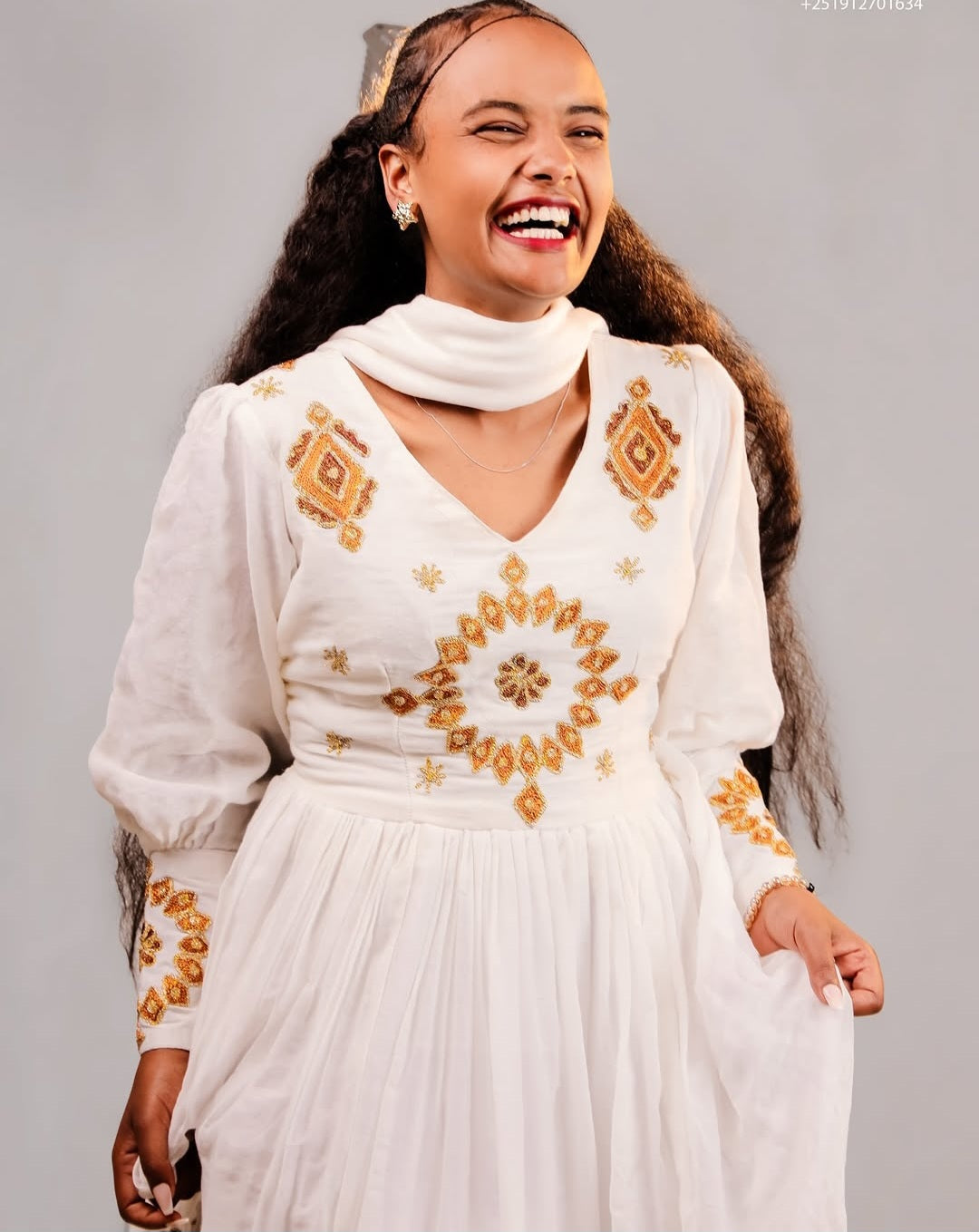 Woman wearing a white Ethiopian traditional dress with gold embroidery against a gray background