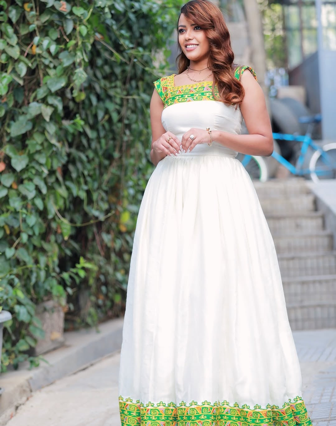 Woman in a white dress with green and yellow accents standing outdoors.