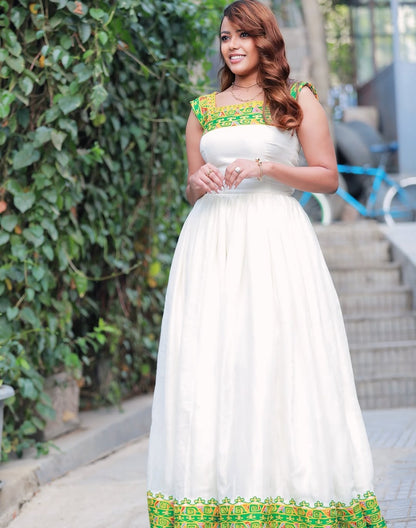 Woman in a white dress with green and yellow accents standing outdoors.