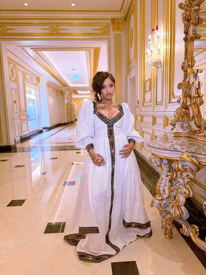 Woman in a white dress with gold accents standing in an opulent hallway.