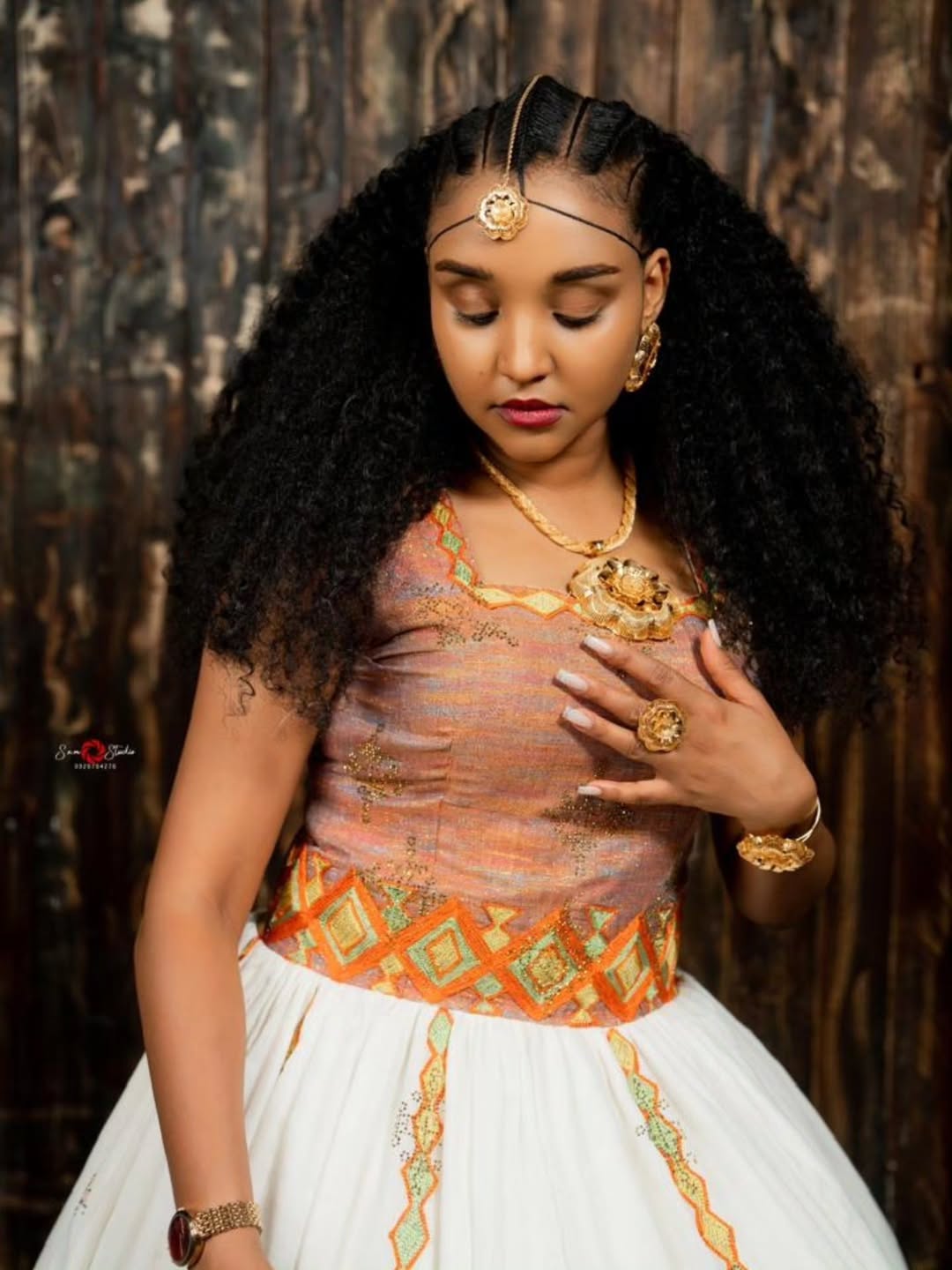 Woman in traditional habesha kemis with intricate jewelry against a dark backgroun