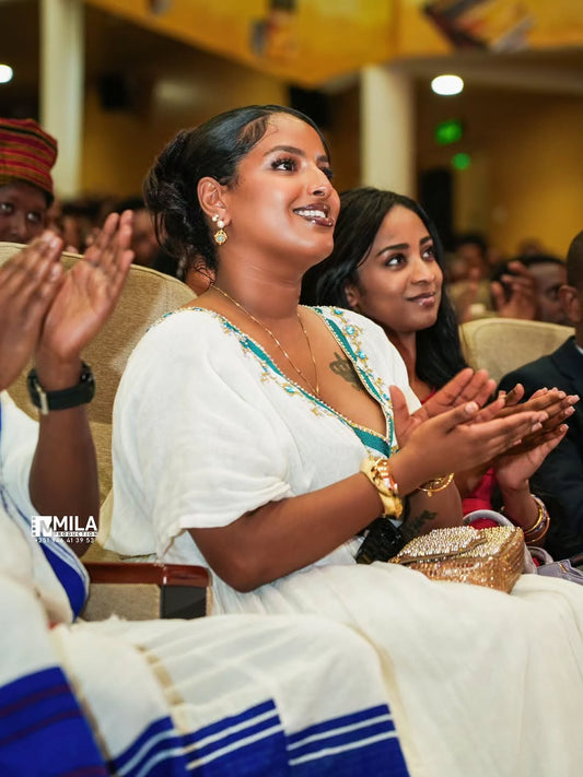 Woman in traditional attire clapping at an event with 'MILA' branding.