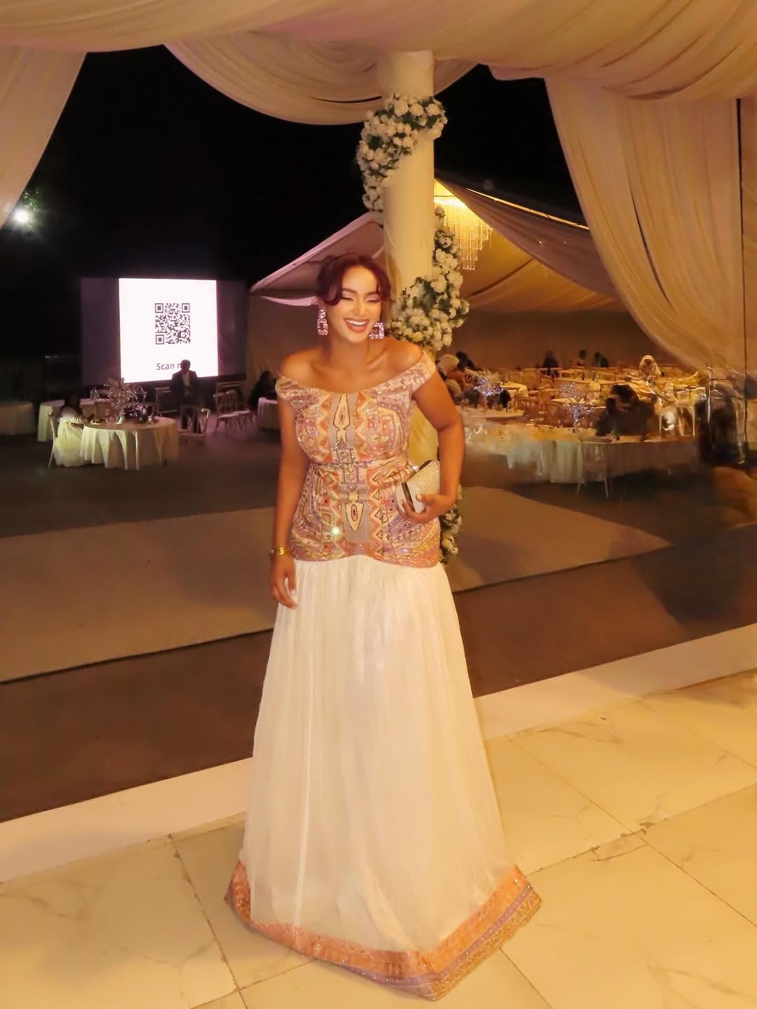 Woman in a decorated tent  Habesha Zuri dress with tables and a screen in the background