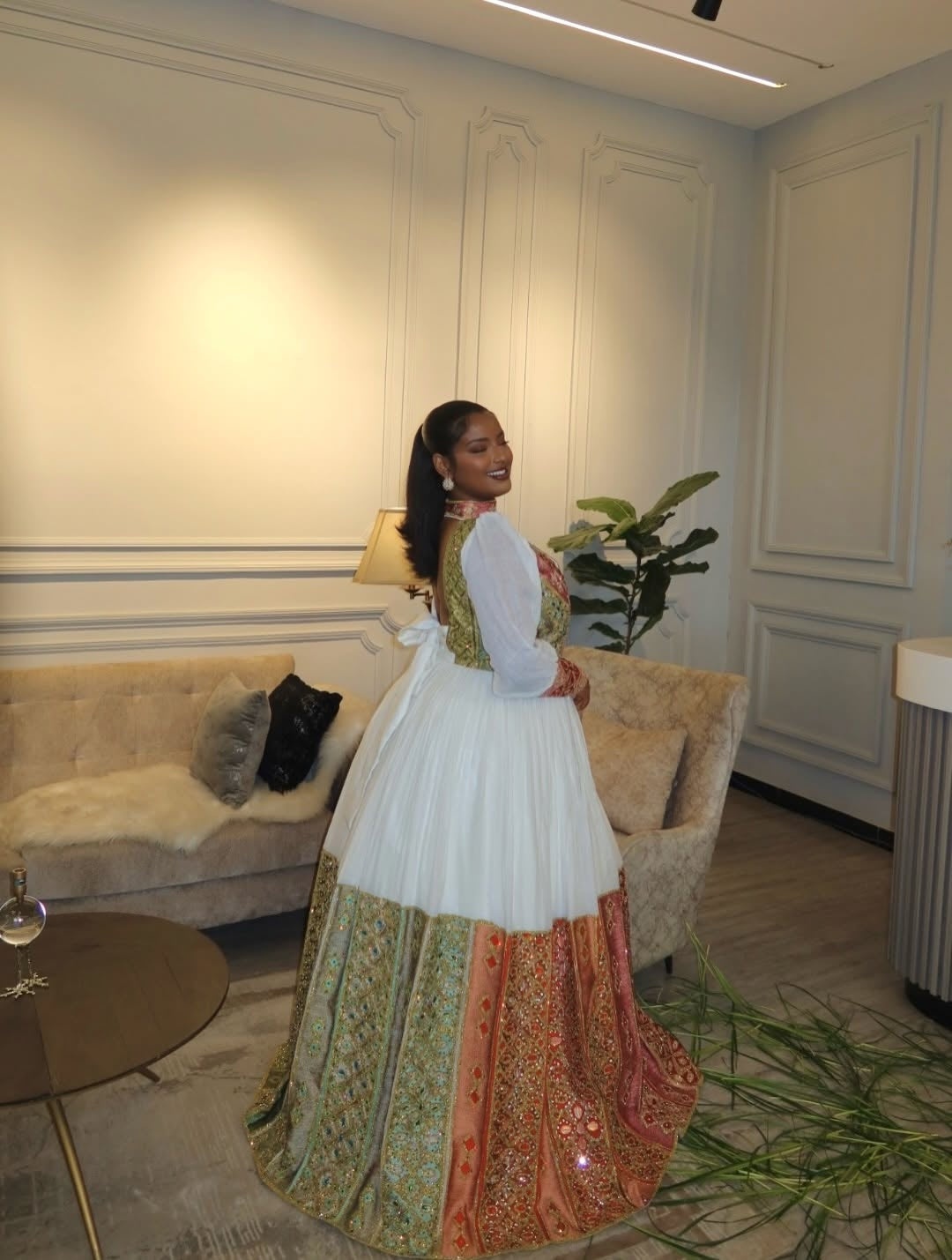 Woman in a traditional Ethiopian dress standing in a stylish living room.
