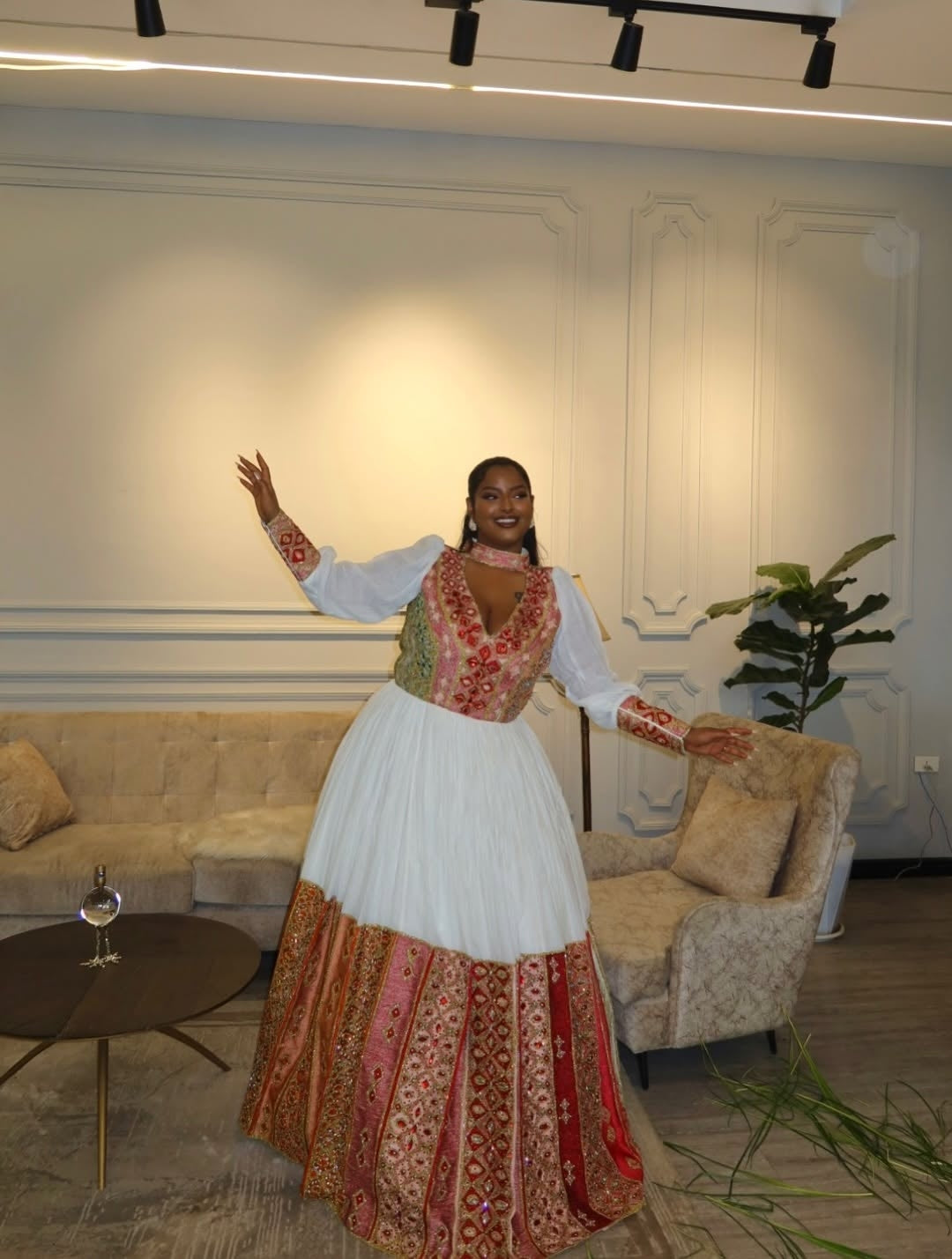 Woman in a traditional Ethiopian dress standing in a modern living room.