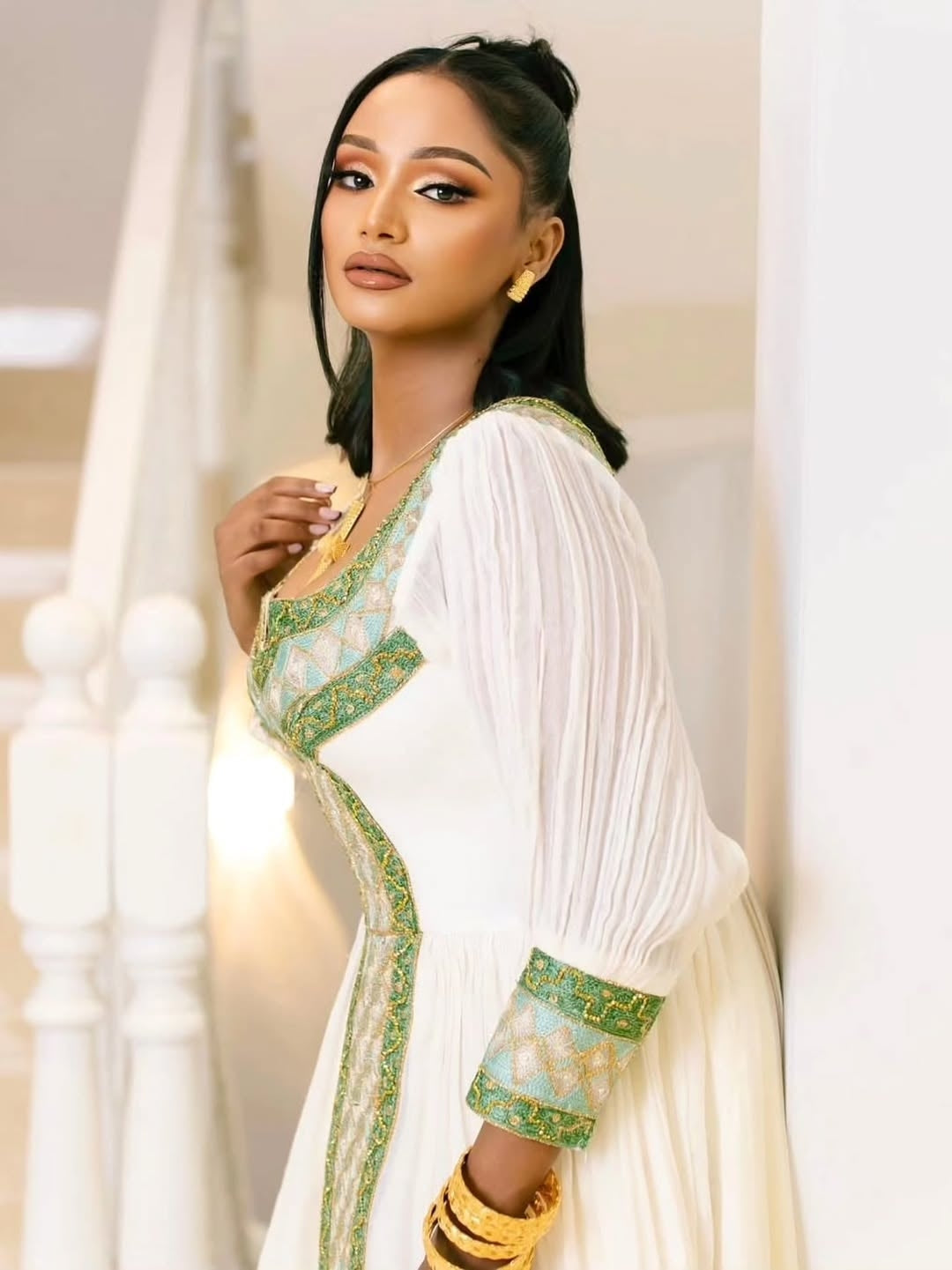 Woman in a white and green traditional Habesha Kemis with gold accents.