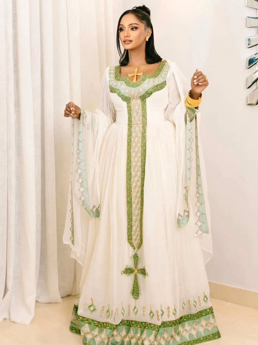 Woman wearing a white and green traditional Habesha Kemis with cross designs.