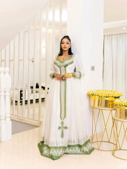 Woman in a white and green traditional Habesha Kemis standing in a modern interior setting.