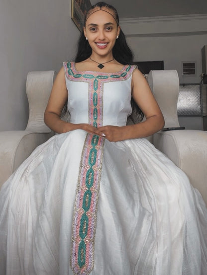 Woman in a white dress with green and pink embroidery sitting on a couch.