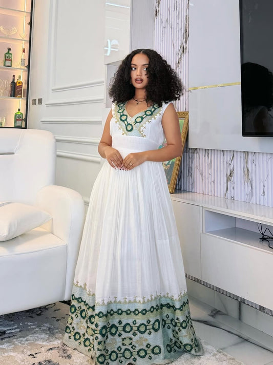 Woman in a white and green habesha dress standing in a living room.
